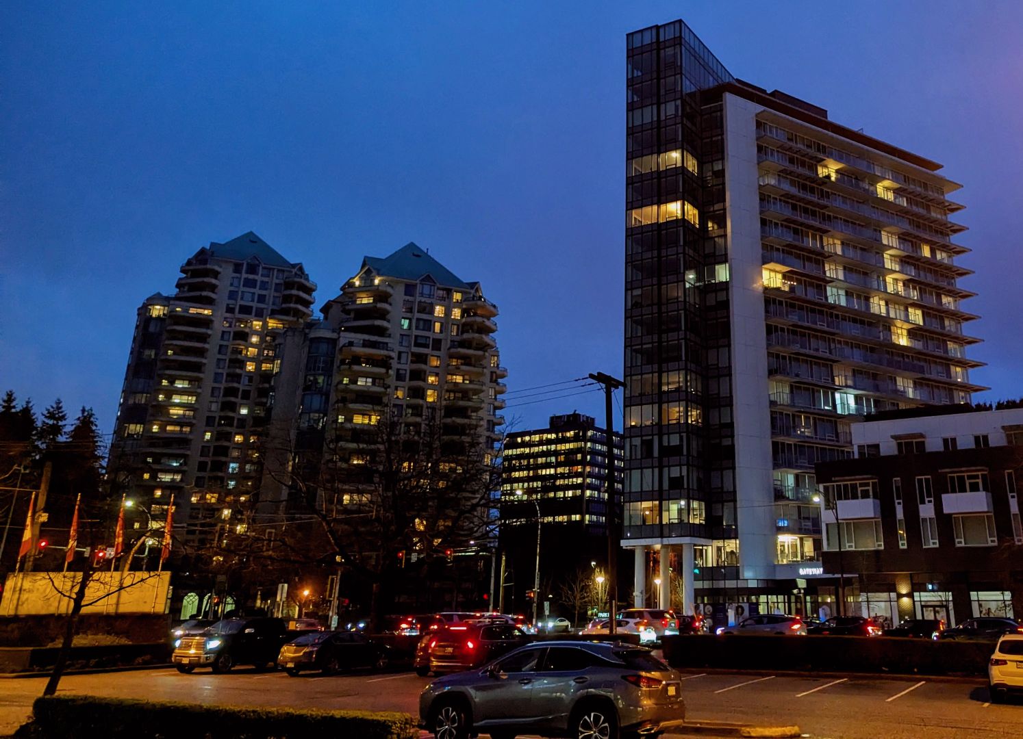 Photo at dusk of two tall buildings on the other side of a relatively empty parking lot. A warm glow lights the scene.